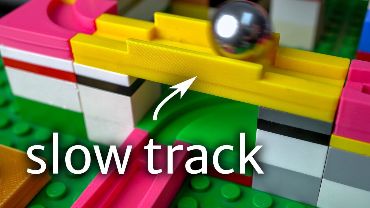 Thumbnail of the youtube video: Several colorful marble run tracks on a green Lego baseplate. Some pieces form a bridge across another track and a shiny ball bearing is rolling across it.