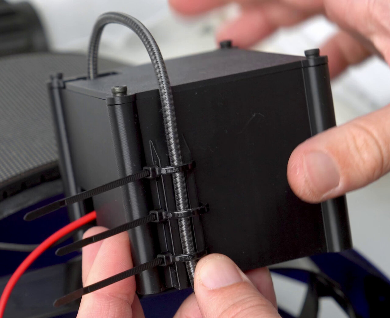 Photo of the 3D-printed case. A USB cable runs out of its top, curves to the front and runs down the side of the case. There three zip ties secure the cable to the case.
